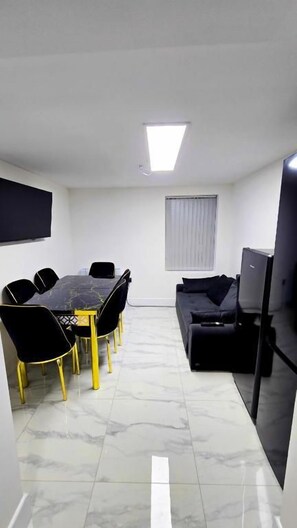 A room with a dining table, chairs, a sofa, a television, and a window with curtains. - Single & Double rooms in Stafford (Stafford)
