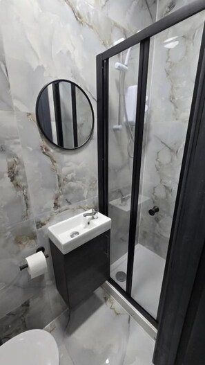 A bathroom with a marble wall, a round mirror, a sink, and a glass-enclosed shower. - Single & Double rooms in Stafford (Stafford)