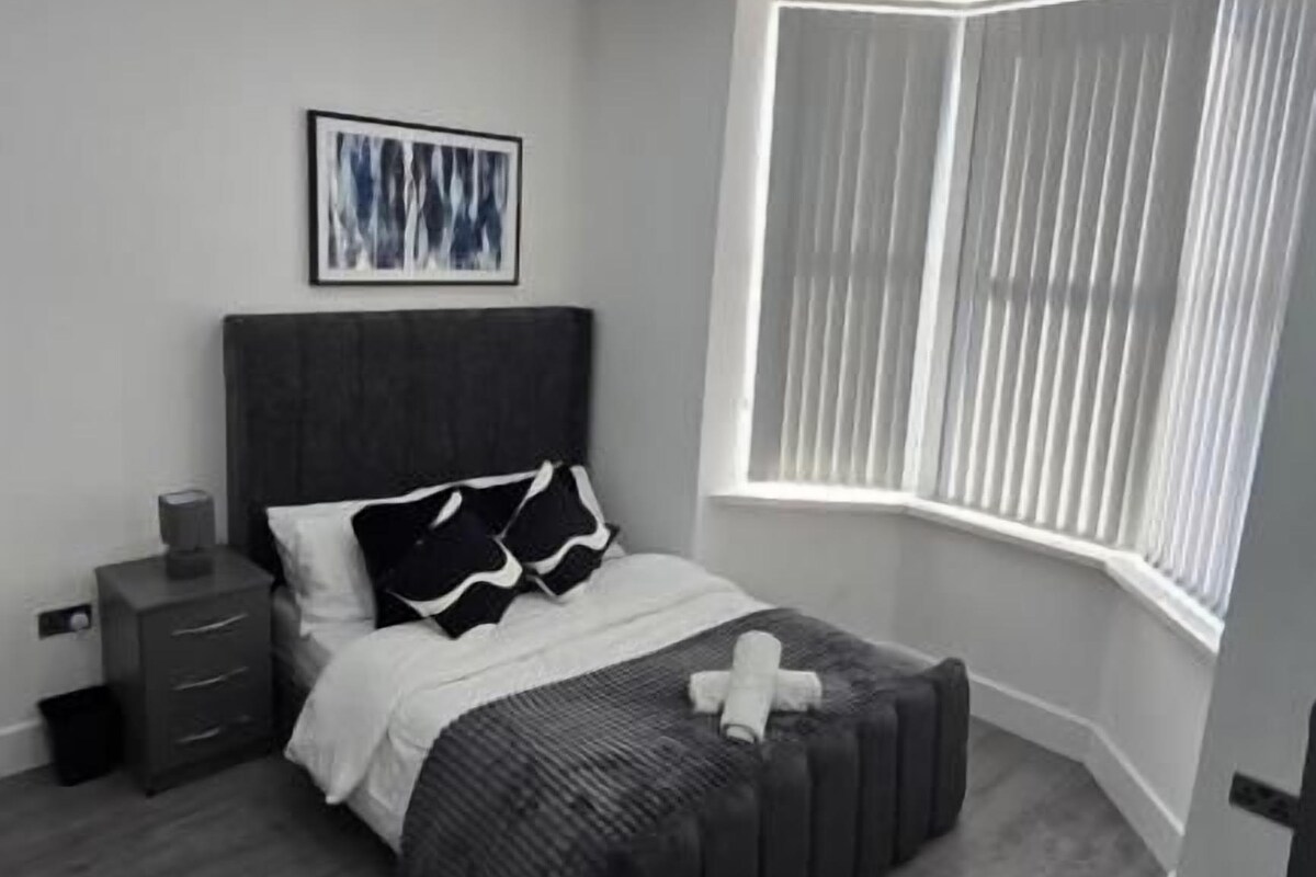 A bedroom with a bed, bedside tables, a window with blinds, and a ceiling light fixture.