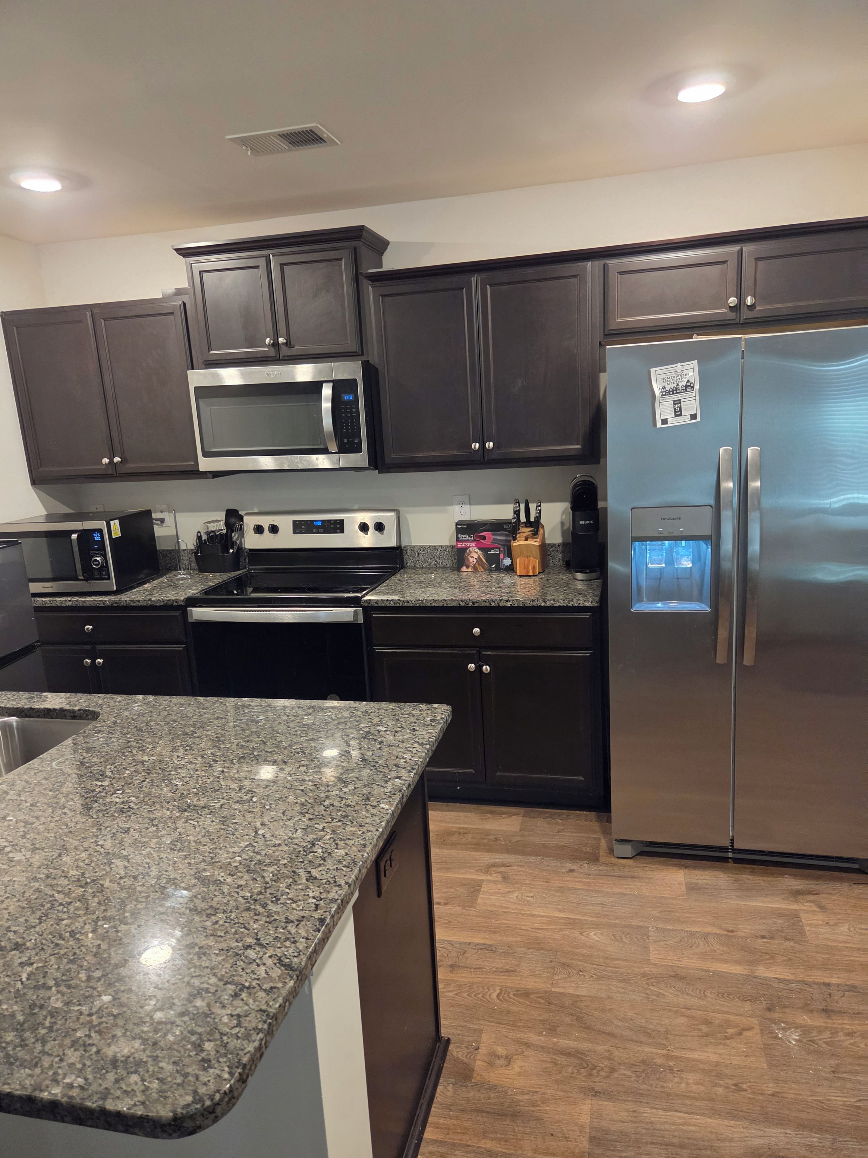 A modern kitchen with dark cabinetry, stainless steel appliances, granite countertops, and a built-in water dispenser.