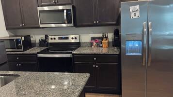 A modern kitchen with dark cabinetry, stainless steel appliances, granite countertops, and a built-in water dispenser.