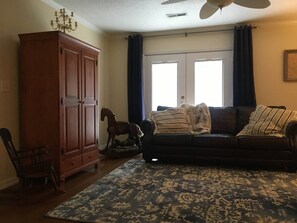 A living room with a dark-colored sofa, a wooden cabinet, a rocking horse, and a patterned rug. - Family-Friendly Retreat Near Charleston (Hanahan)