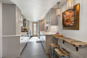 A narrow kitchen with modern appliances, a wooden bench, and a painting on the wall. - Downtown | On Bus Route | Garage Gear Storage | Pet Friendly (Steamboat Springs)