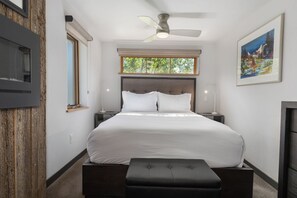 Ein Schlafzimmer mit Bett, Deckenventilator, Fenster, einem Gemälde und einem Nachttisch.