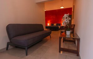 A modern living room with a sofa, a dining table with chairs, and a red accent wall. - Casa Marmorata | Residence with Air Conditioning and Parking (Oaxaca de Juárez)