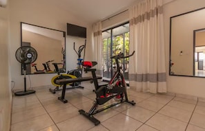 A home gym with exercise equipment, a standing fan, and a large window with curtains. - Casa Marmorata | Residence with Air Conditioning and Parking (Oaxaca de Juárez)