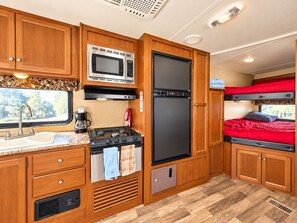 A compact RV kitchen with a stove, microwave, refrigerator, sink, and a small window. - Cozy RV Getaway in Sturgis Private Bedroom Bunk beds Full Kitchen (Sturgis)