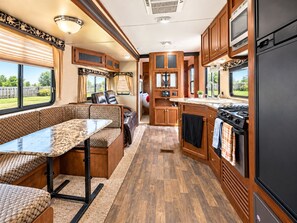 A compact RV interior with a dining area, kitchenette, and a small sleeping space. - Cozy RV Getaway in Sturgis Private Bedroom Bunk beds Full Kitchen (Sturgis)
