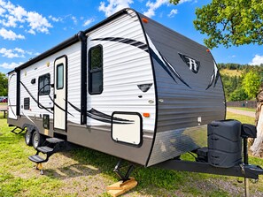 A stationary RV with a side entrance, a small attached kitchen area, and a storage compartment. - Cozy RV Getaway in Sturgis Private Bedroom Bunk beds Full Kitchen (Sturgis)