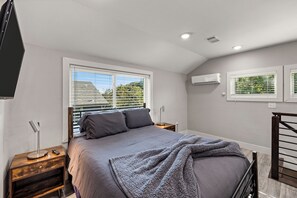 Une chambre à coucher comprenant un lit, des tables de chevet, un appareil de climatisation et une fenêtre avec des stores.