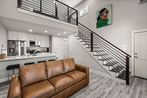 A modern kitchen with stainless steel appliances, a dining area with a brown leather sofa, and a staircase with a metal railing. - Carriage House: No Cleaning/Pet Fees Soaking Tub Pet Friendly (Galveston)