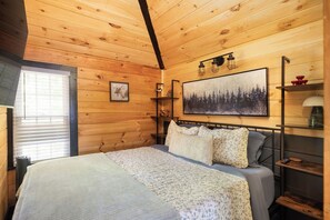 Ein Zimmer mit Holzwandverkleidung, einem Bett, einem Gemälde und einem Fenster mit Jalousien.