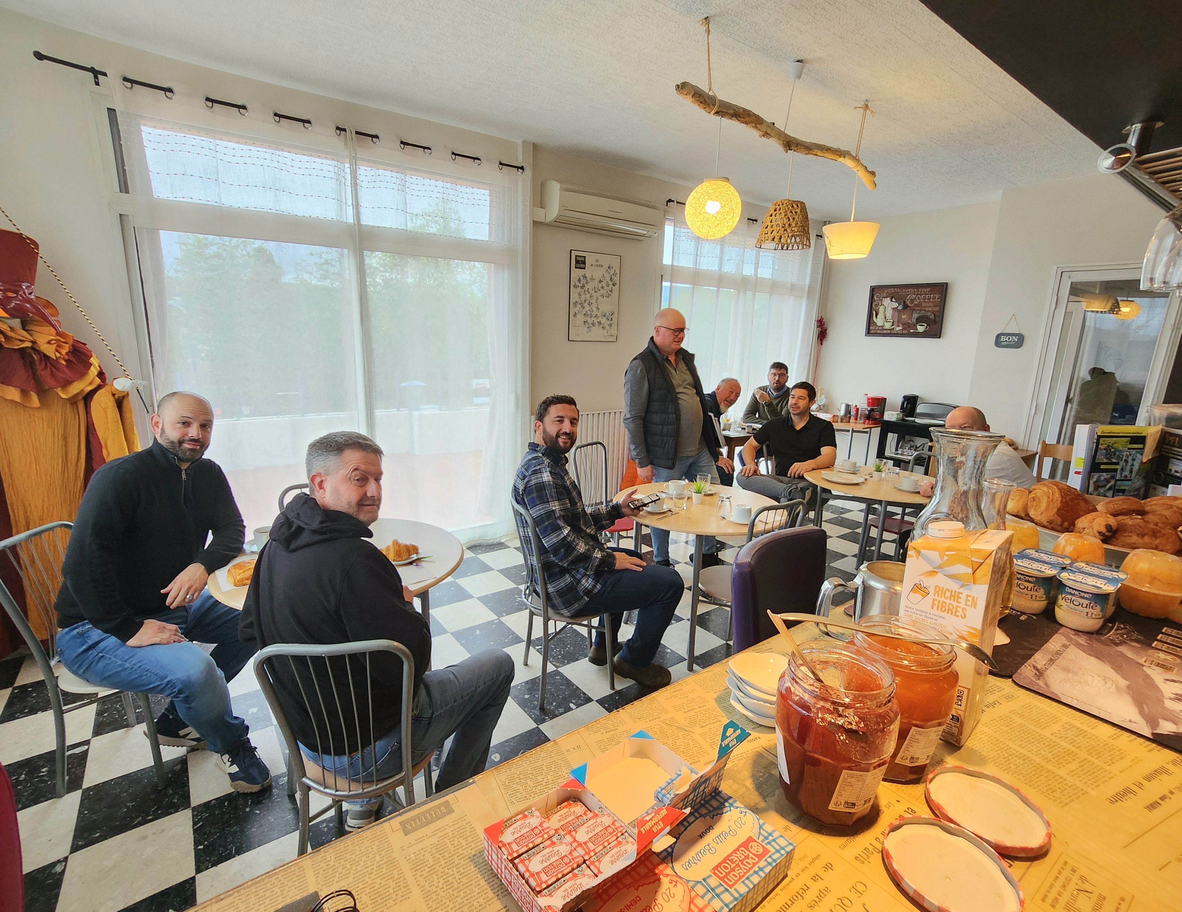 Un café au sol carrelé, avec des tables où sont servis des plats pour le petit-déjeuner et des lampes suspendues.