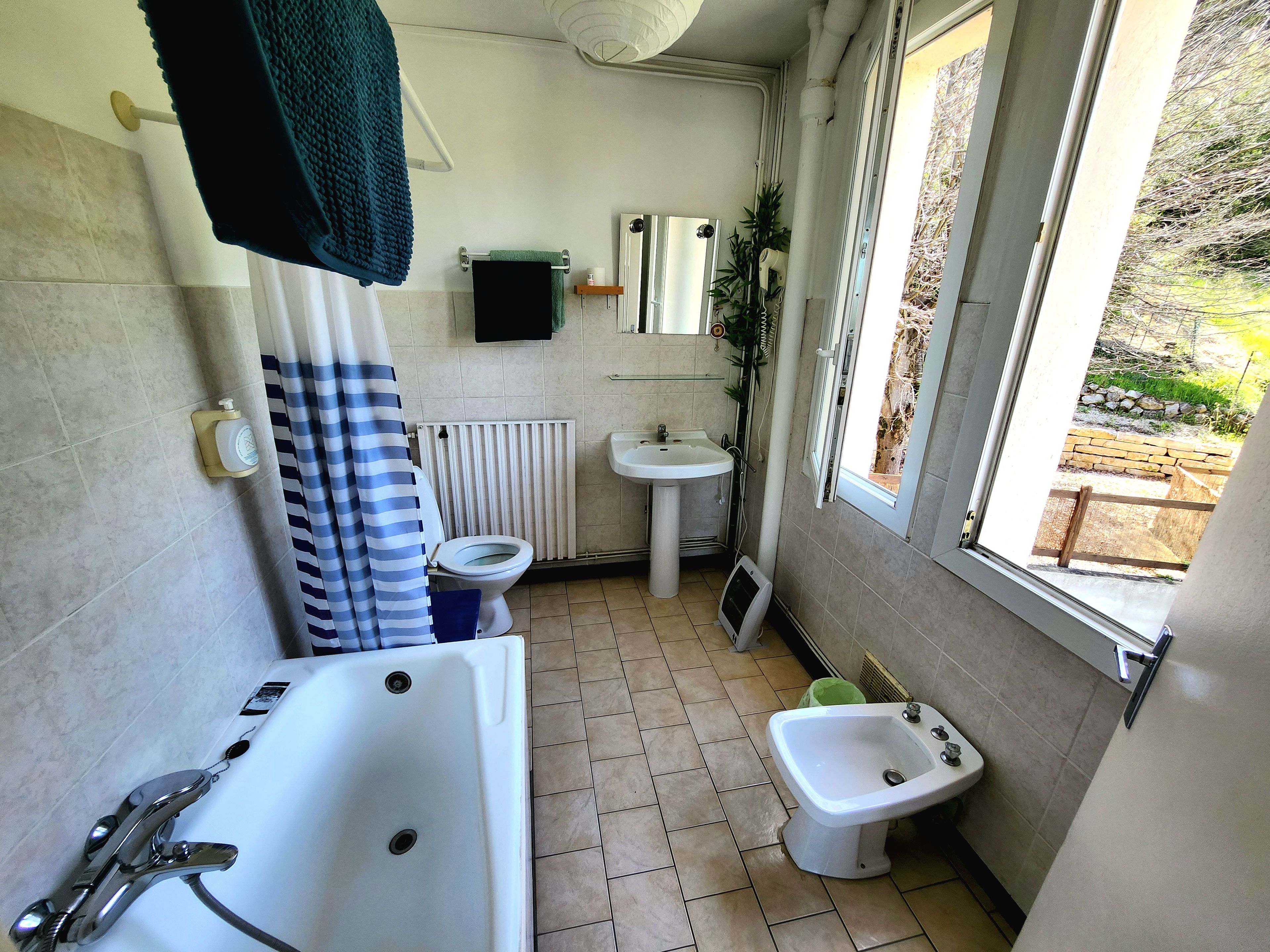 Une salle de bain équipée d’une baignoire, de toilettes, d’un bidet, d’un lavabo et d’une fenêtre donnant sur l’extérieur.