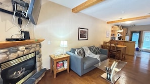 A living room with a fireplace, a sofa, a coffee table, and a dining area with wooden furniture. - 2-Bedroom Townhouse Near Banff Gate (Harvie Heights)