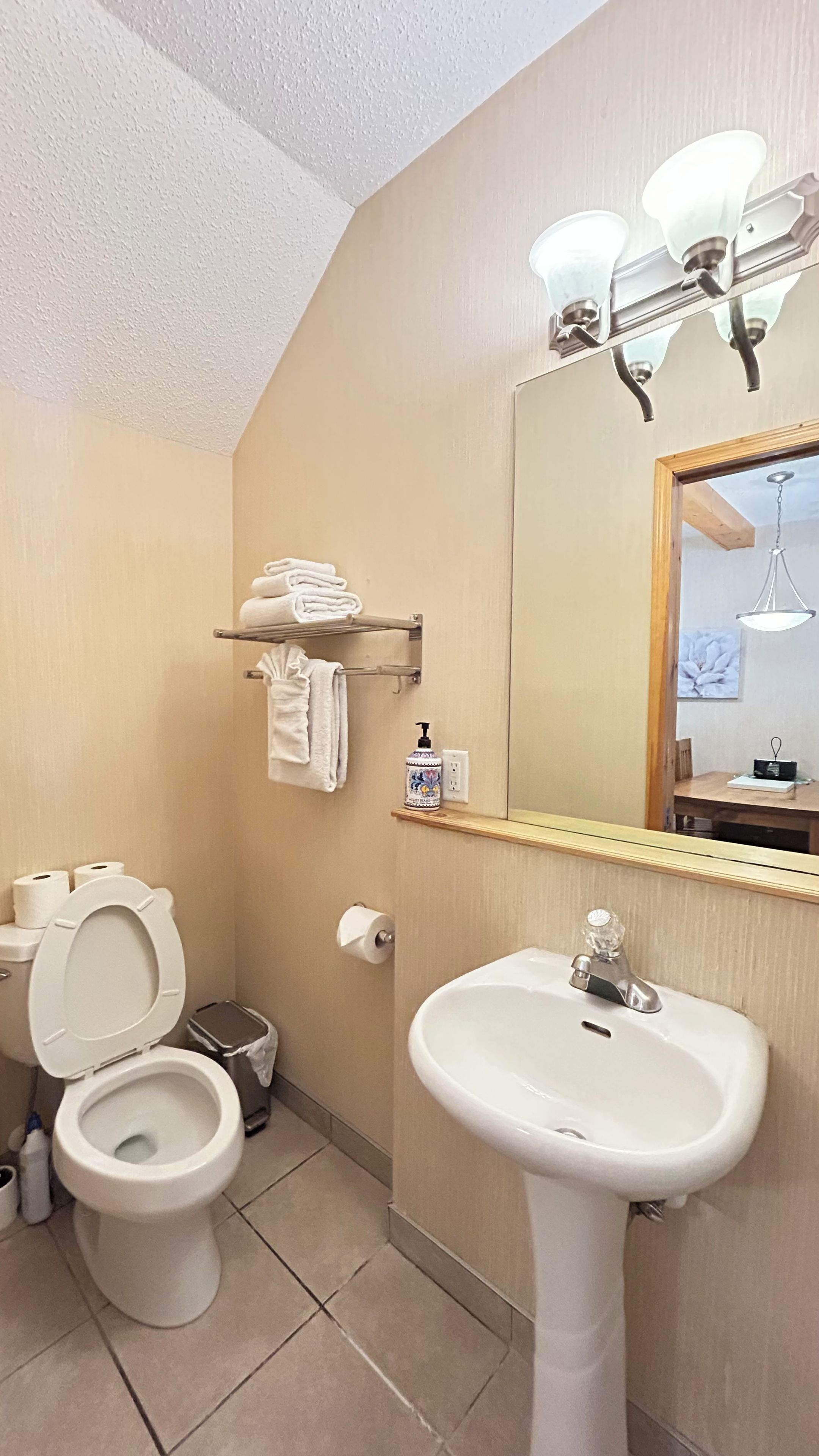 A bathroom with a toilet, sink, towel rack, and a mirror with lights.