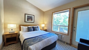 A hotel room with a bed, two bedside lamps, a framed picture on the wall, and a large window with a view of trees. - 2-Bedroom Townhouse Near Banff Gate (Harvie Heights)
