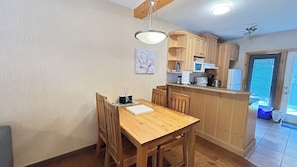 A compact kitchen with wooden cabinets, a dining table, and chairs. There is a microwave, a kettle, and a coffee maker on the counter. - 2-Bedroom Townhouse Near Banff Gate (Harvie Heights)