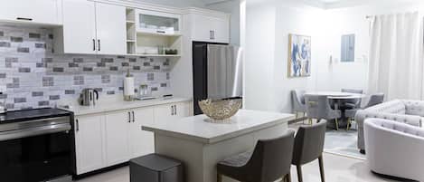 Une cuisine moderne avec des armoires blanches, un réfrigérateur noir et un mur recouvert de carreaux. On y trouve également un coin repas avec une table ronde et des chaises.