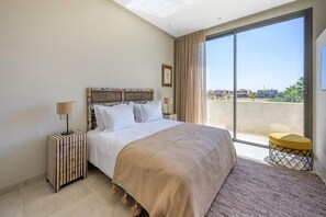 A hotel room with a large bed, a bedside table, a lamp, a window with a view, and a small stool. - Modern 4-bedroom villa with a pool and hot tub - Golf Community (Marrakech)