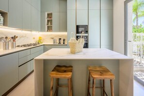 A modern kitchen with a marble countertop, wooden stools, and a woven basket on the island. - Modern 4-bedroom villa with a pool and hot tub - Golf Community (Marrakech)