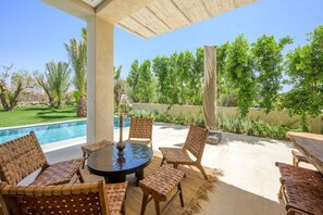 An outdoor patio with a round table and wicker chairs, overlooking a swimming pool and lush greenery. - Modern 4-bedroom villa with a pool and hot tub - Golf Community (Marrakech)