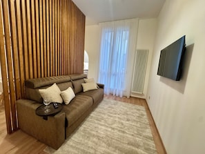 Ein Wohnzimmer mit einem braunen Sofa, einem Weinglas, einer Fernbedienung und einem Fernseher an der Wand.