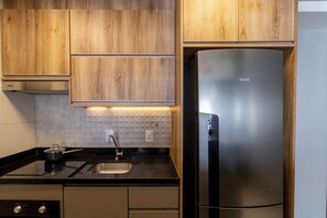 A modern kitchen with wooden cabinets, a stainless steel refrigerator, a black countertop, and a sink with a faucet. - Maia Supreme Apartment 012207 5 min Shopping Maia (Guarulhos)