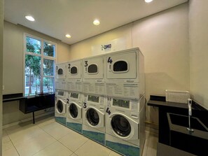 A laundry facility with four washing machines and dryers, a sign above indicating 'KOMO', and a window providing a view of the outdoors. - Maia Supreme Apartment 012207 5 min Shopping Maia (Guarulhos)