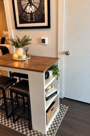 A modern interior with a dining area featuring a wooden table and black chairs, a white shelving unit with decorative items, and a large clock on the wall. - Cozy 1-bed Midtown apartment ATL STAY Walkable and Central location (atlanta)