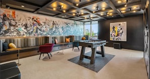 Zona d'estar moderna amb taula de futbolí, seients confortables i un mural gran a la paret.