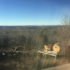 A wooden deck with a sauna and a bench, surrounded by trees and a view of the landscape.