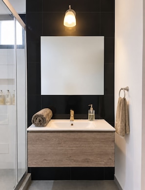 A modern bathroom with a large mirror, a wooden vanity, a towel rack, and a glass shower enclosure. - The City Condos Playa del Crmen (gonzalo Guerrero)