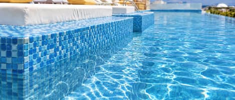 A swimming pool with clear blue water, tiled steps, and lounge chairs with cushions.