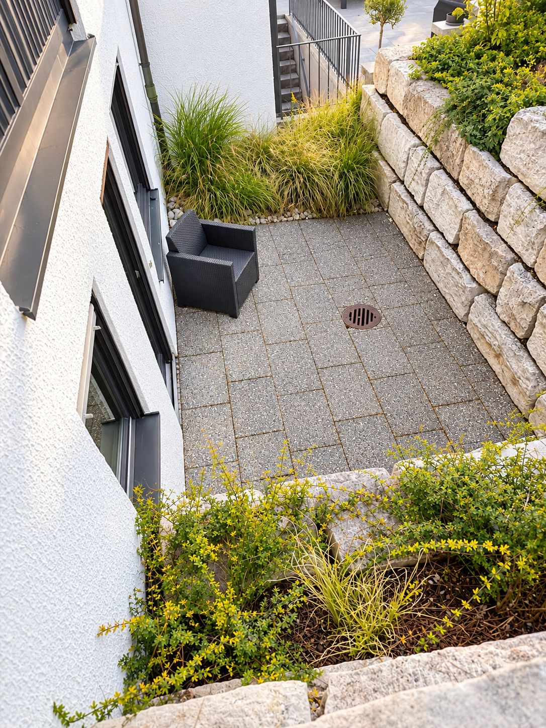 A modern outdoor patio area with a stone floor, a black outdoor seating area, and a stone retaining wall.