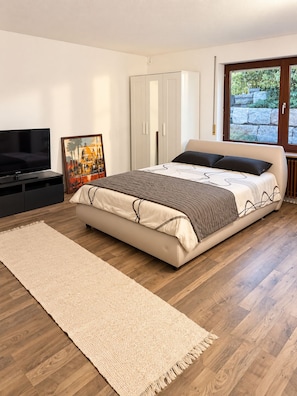 A bedroom with a bed, a television, a painting, a wardrobe, and a window with a view. - Bright 1-bedroom apartment with a terrace – quiet location (Korb)