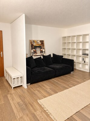 A room with a black sofa, a white bookshelf, and a wooden floor. - Bright 1-bedroom apartment with a terrace – quiet location (Korb)