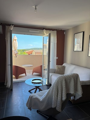 A room with a bed, a chair, a glass table, and a view of a balcony with outdoor furniture. - Air-conditioned apartment, free underground parking (Sanary-sur-Mer)