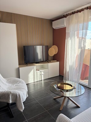 A modern living room with a flat-screen TV, a round glass coffee table, and a white sofa. - Air-conditioned apartment, free underground parking (Sanary-sur-Mer)