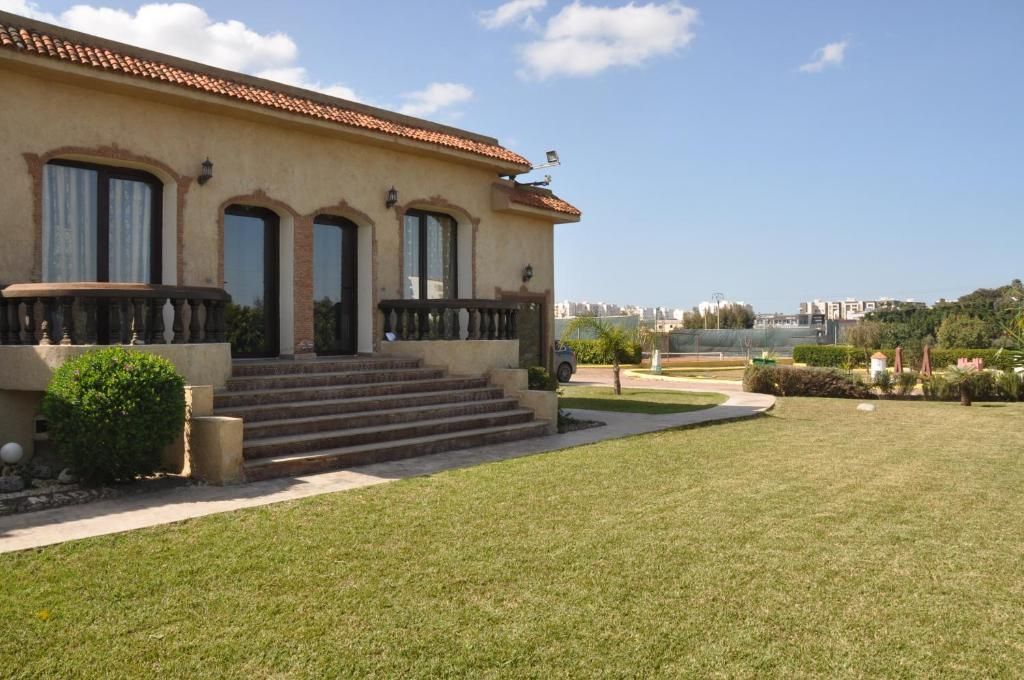 A two-story building with a tiled roof, a front porch with steps, and a view of the cityscape in the background.