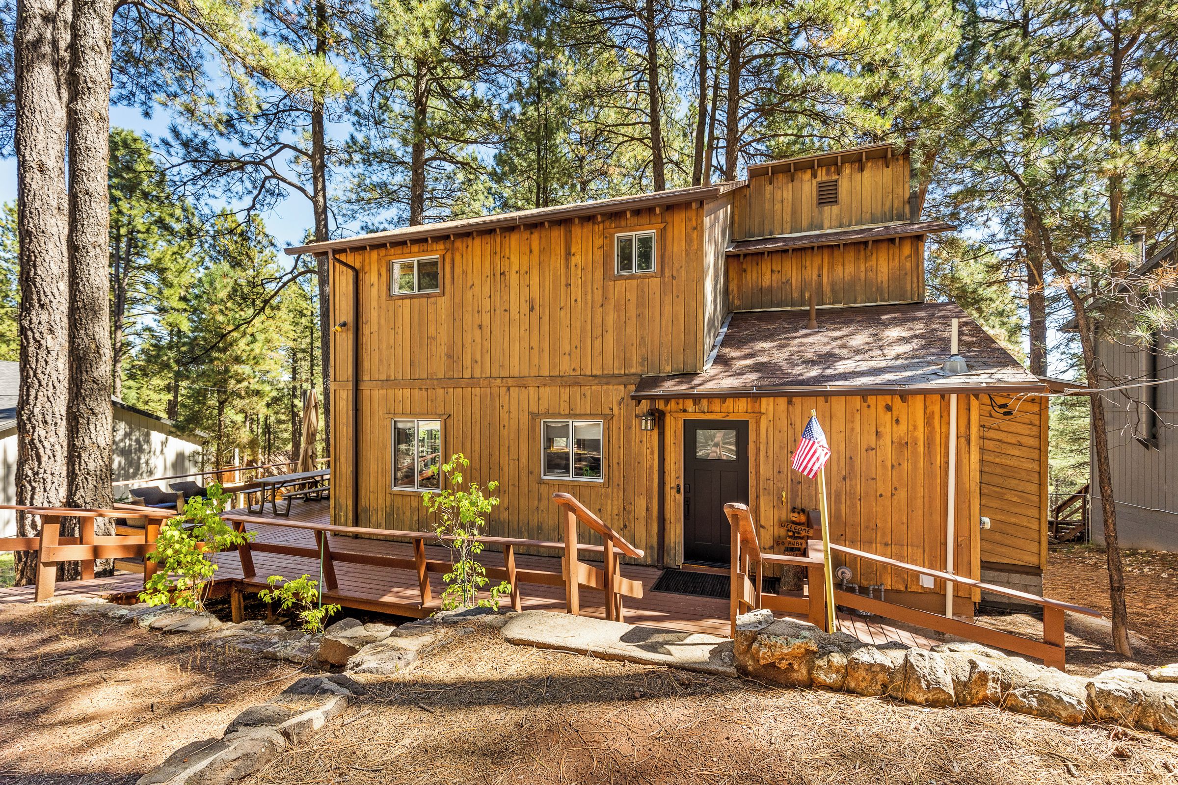 A two-story wooden cabin with a front porch, a small attached shed, and a flag.