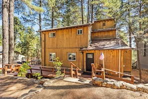 A two-story wooden cabin with a front porch, a small attached shed, and a flag. - Ping-Pong & Games with Porch Meals and Outdoor Fun (Flagstaff)