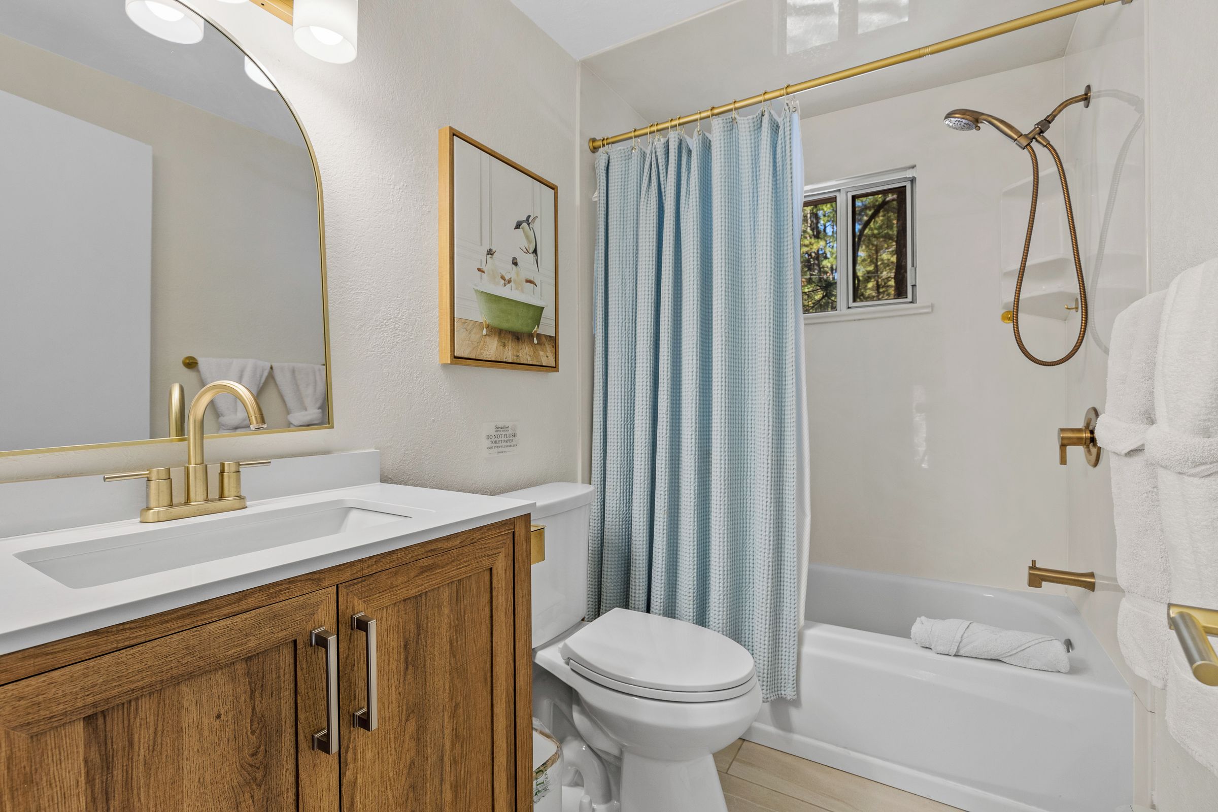 Een badkamer met een witte wastafel, gouden kraanwerk, een houten kastje, een wit toilet, een bad met douchekop en een blauw douchegordijn.