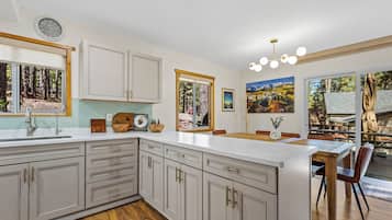 Een moderne keuken met een groot eiland, houten vloeren en een eethoek met uitzicht op de omgeving.
