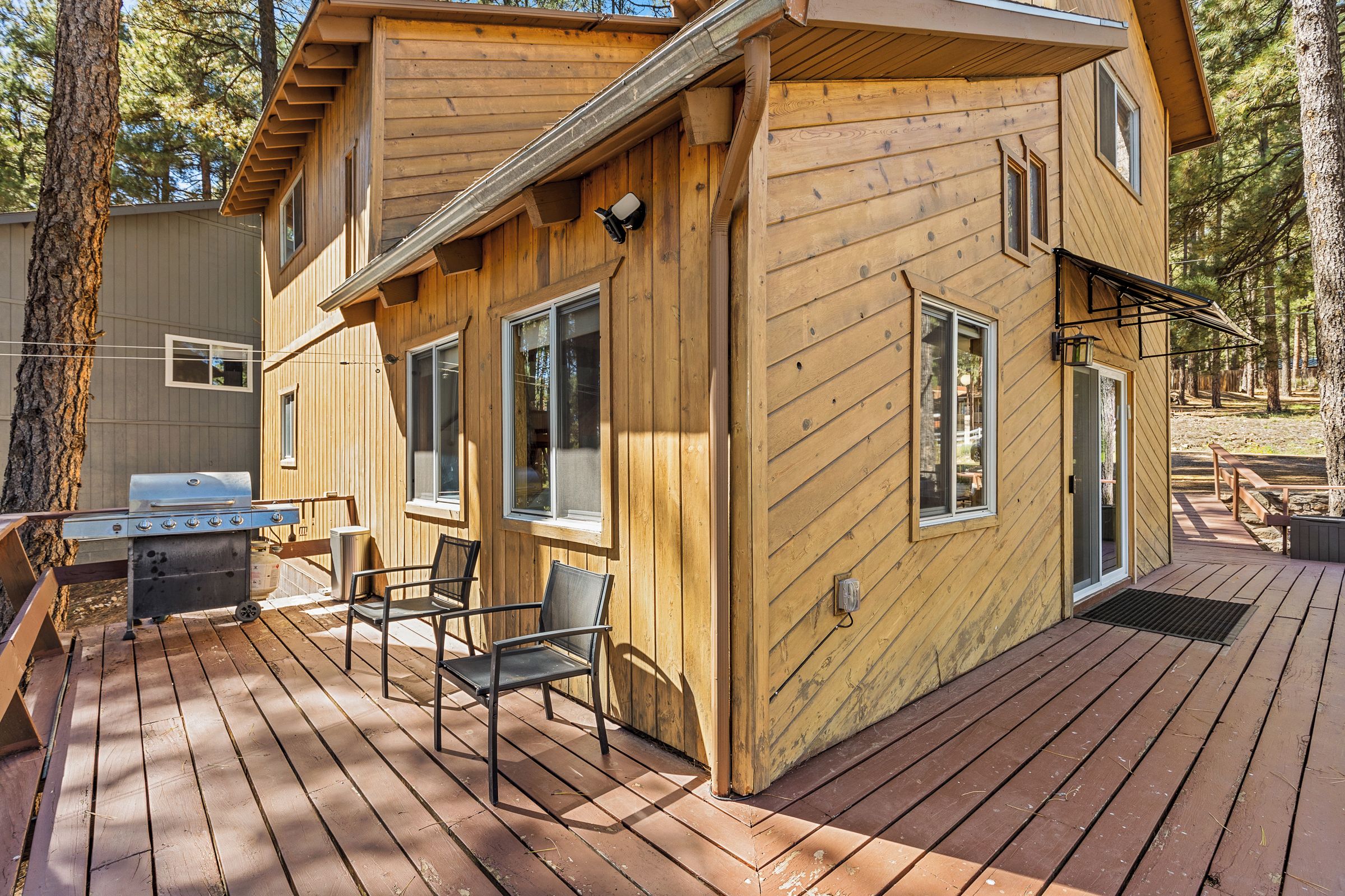 Una cabaña de madera con terraza, una parrilla y una silla.