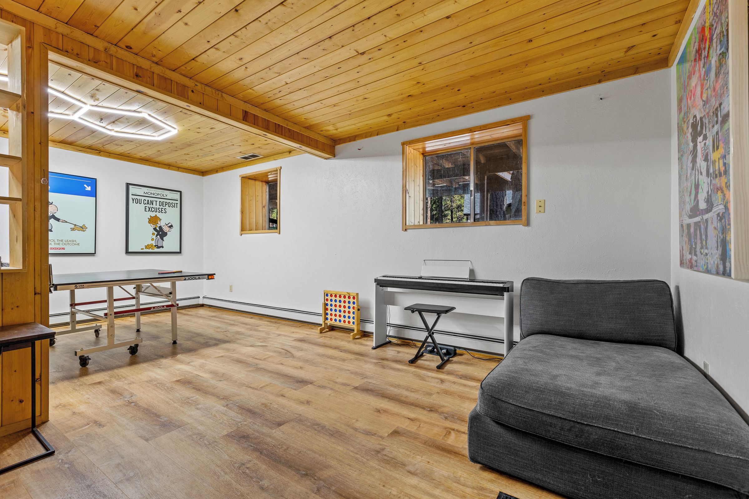 Una habitación con techo de madera, un sofá gris, un escritorio y una mesa con un cartel.