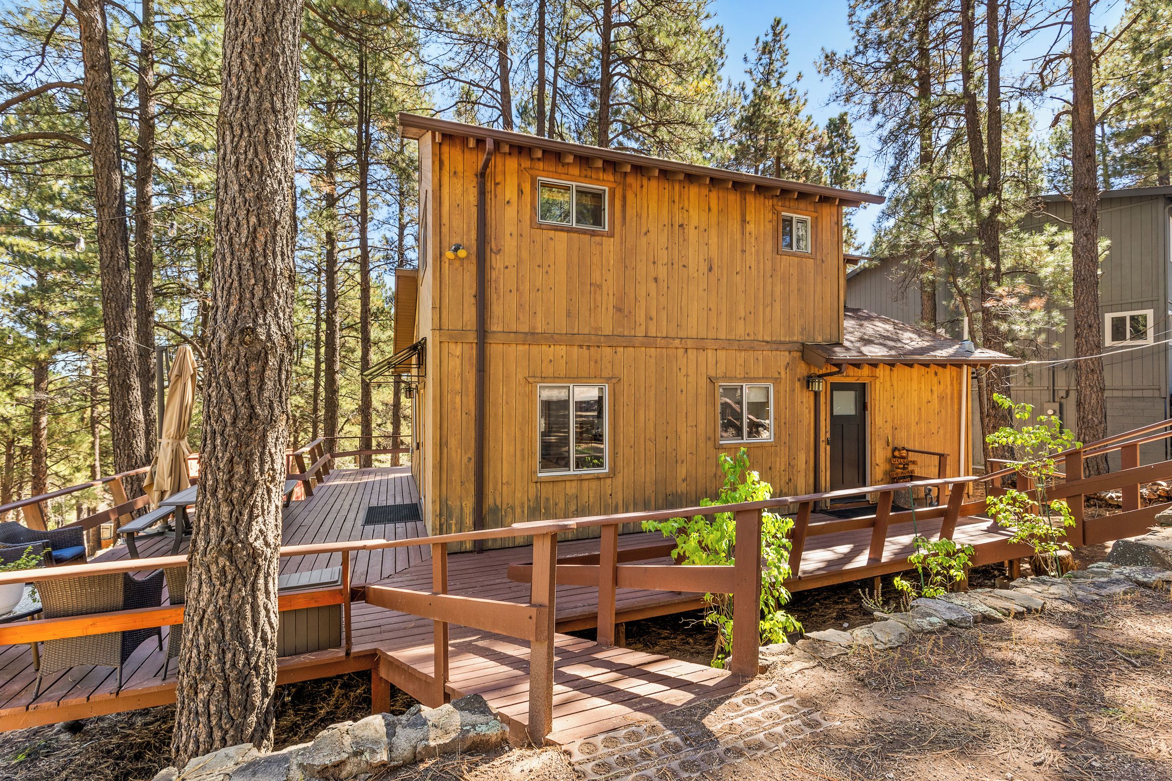 A wooden cabin with a deck, surrounded by trees.