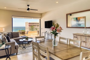 A spacious living area with a balcony overlooking the sea, a dining table, and a TV mounted on the wall. - Family Friendly Apt- 17 Ocean View, 3br, 6 pax (Cabo San Lucas)