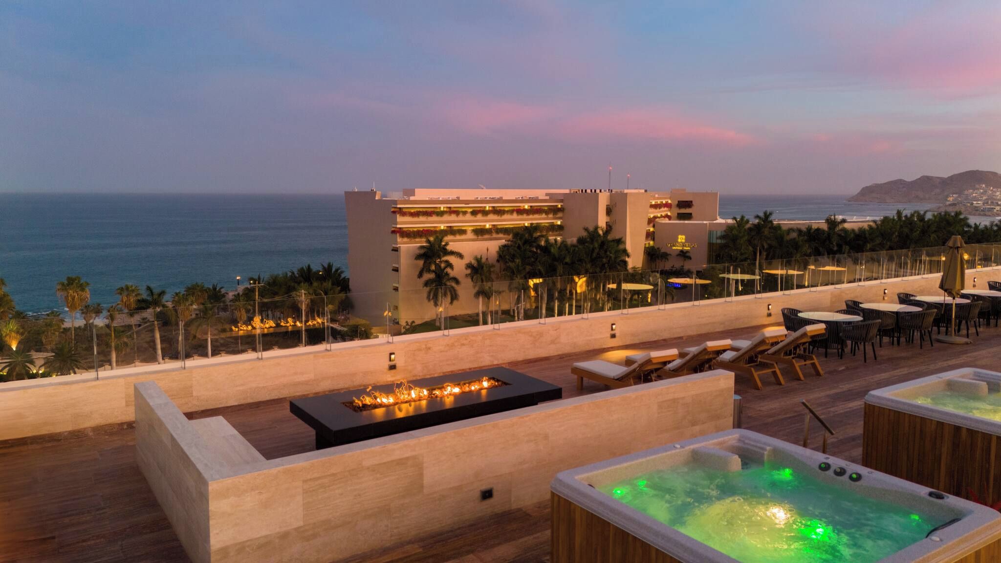 A rooftop terrace with a pool, lounge chairs, and a view of the ocean and a hotel building.