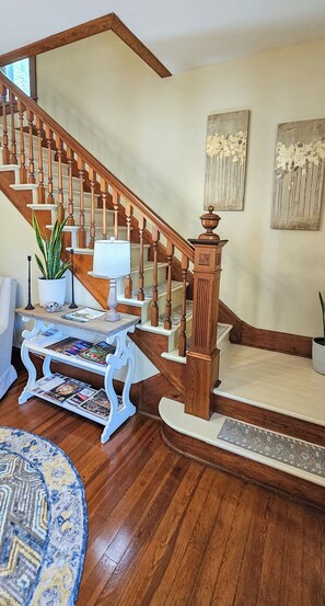 A wooden staircase with a white carpeted landing, a white table with magazines, a potted plant, and a blue patterned rug. - Historic Bed & Breakfast 8 Bedrooms, Groups/family (Eureka Springs)